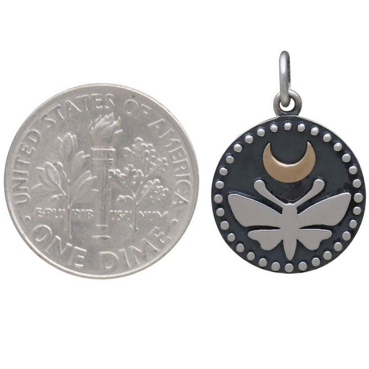 A US dime sits next to Nina Designs’ Sterling Silver Moth Charm, featuring a luna moth with a bronze moon and dot accents along the round pendant’s edge.