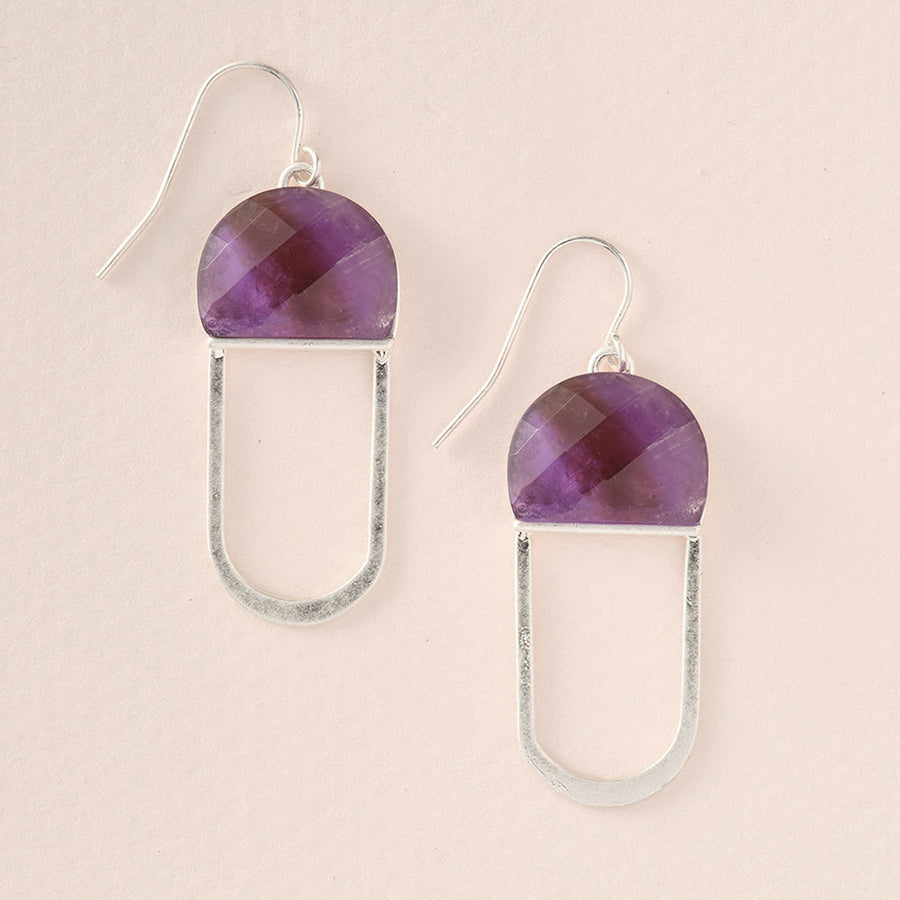 The Modern Stone Earring Amethyst Silver by Scout Jewelry features elegant half-circle purple amethyst stones and silver open oval shapes on a light beige background, with each earring hanging from a delicate, hypoallergenic hook suitable for sensitive skin.