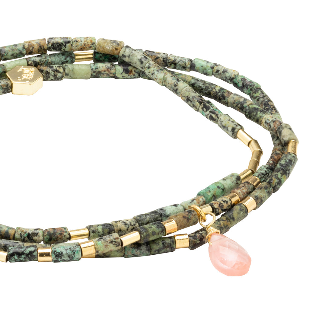 The Transformation African Turq Gold Teardrop Wrap by Scout Jewelry features African turquoise and black speckled beads, gold accents, and a pink teardrop stone pendant on one strand.
