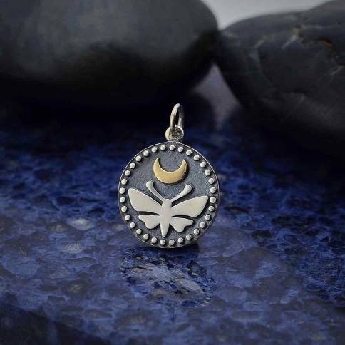 The Nina Designs Sterling Silver Moth Charm with Bronze Moon and Do features a luna moth under a bronze crescent moon within a dotted border, reflecting Victorian Era mystique, shown atop blue stone for an enchanting effect.