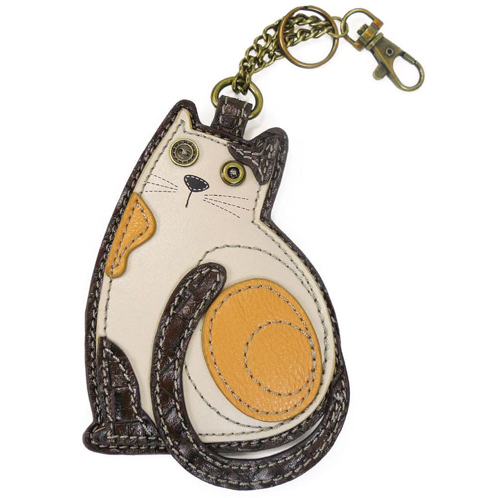 The Cat Keychain with Zip by Chala is a leather keychain crafted in the shape of a sitting cat, showcasing brown, orange, and cream patches. It features button eyes, a meticulously stitched outline, and is complemented with antique brass hardware for the chain and clasp at the top.