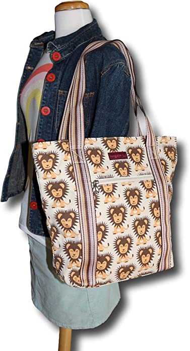 A mannequin wears a denim jacket, graphic tee, and light skirt, carrying the Bungalow 360 Striped Tote - Lion, a roomy cotton canvas bag featuring unique cartoon lion faces and striped shoulder straps.