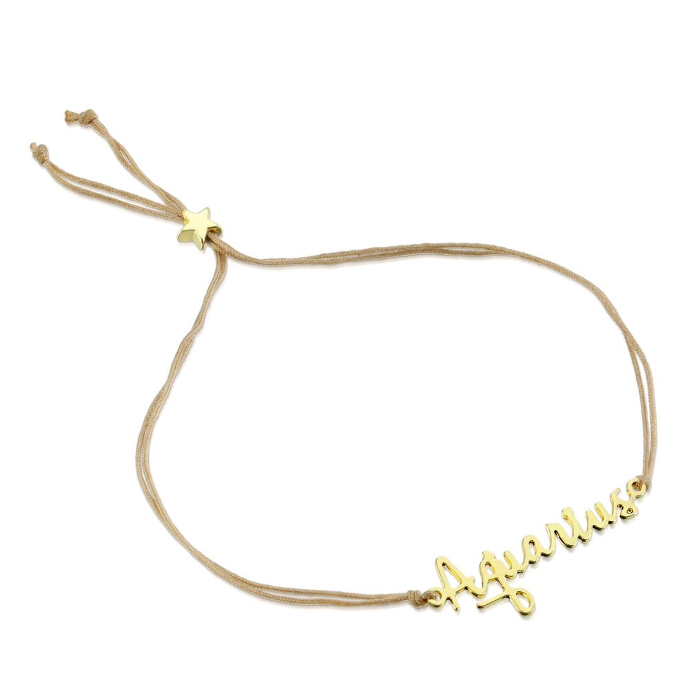 The LuckyFeather Zodiac Bracelet Aquarius features a beige cord with a nickel-free, 14k gold-dipped "Aquarius" charm in cursive, an adjustable sliding knot, and a small star accent.