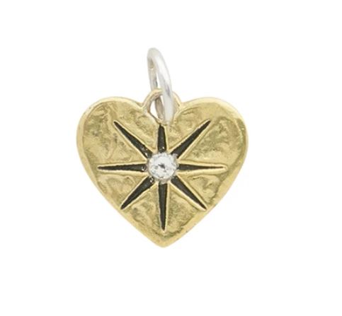 The Waxing Poetic guided by heart compass pendant is a gold brass heart with a textured surface, showcasing a black eight-pointed compass rose and a clear Kristal crystal at the center, plus a loop for attaching to a chain.