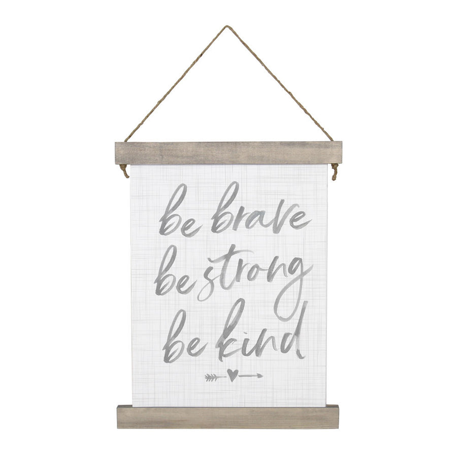 The "Be Brave" wall hanging by SincereSurroundings features handwritten phrases "be brave, be strong, be kind" in gray on a light grid background. It is framed with stained wood and hangs from a simple rope, with a small arrow and heart adorning the design.