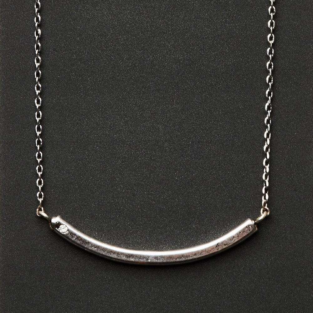 The Refined Neck Comet/Silver by Scout Jewelry is a minimalist piece with a curved bar-shaped pendant crafted from 925 silver. Its delicate chain enhances the sleek, polished look set against a dark background.