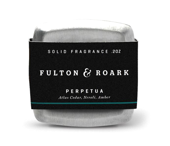 A silver tin with a black band labeled "Fulton & Roark" features "Perpetua .2oz," offering notes of cedarwood, neroli, and amber for a rich fragrance experience.