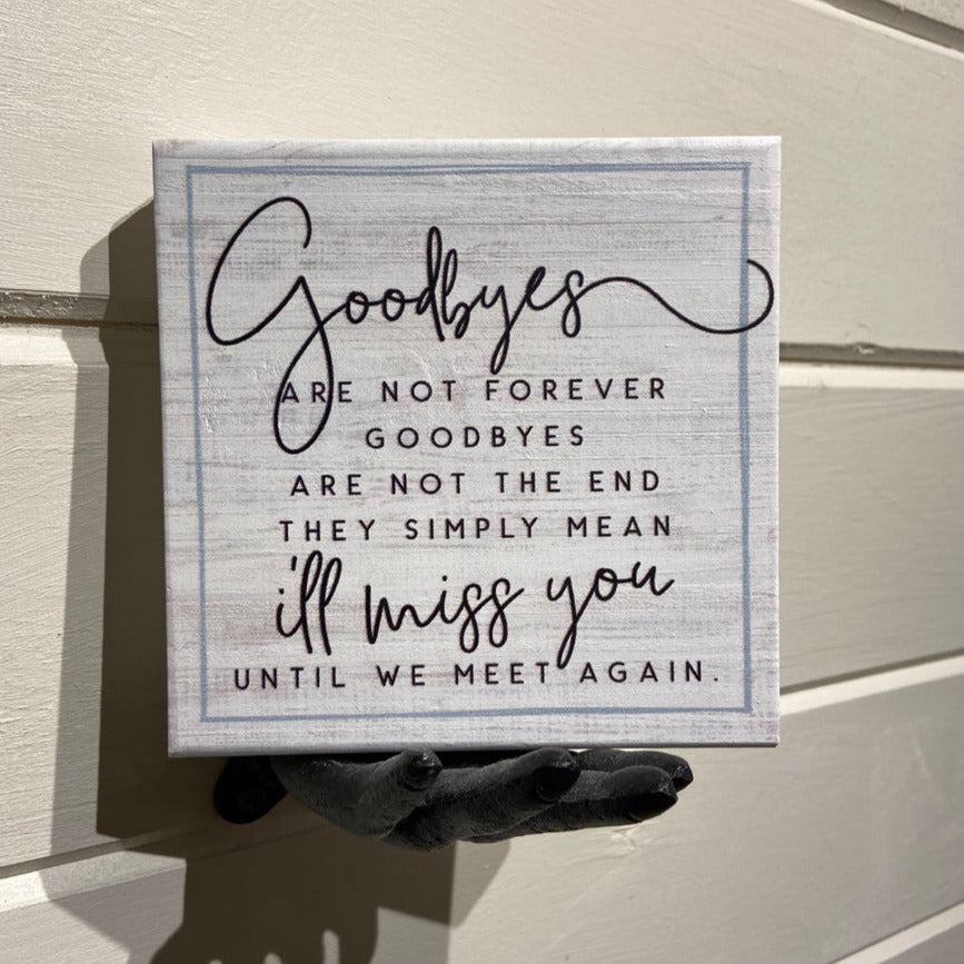 A SincereSurroundings handcrafted sign named "Goodbyes" is displayed on a wooden wall, featuring the heartfelt message: "Goodbyes are not forever, goodbyes are not the end. They simply mean I'll miss you until we meet again." The elegant and handwritten font mix makes it an ideal piece for any shelf display.