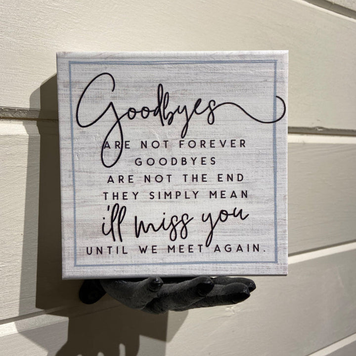 A SincereSurroundings handcrafted sign named "Goodbyes" is displayed on a wooden wall, featuring the heartfelt message: "Goodbyes are not forever, goodbyes are not the end. They simply mean I'll miss you until we meet again." The elegant and handwritten font mix makes it an ideal piece for any shelf display.