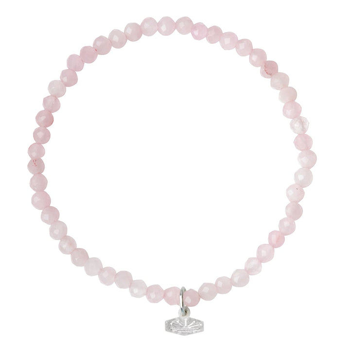 Experience the elegance of the Mini Bracelet Rose Quartz/Silver by Scout Jewelry. This delicate bracelet features small, round rose quartz beads strung together on a stretch cord, creating an elegant design. A small silver charm with an etched leaf pattern dangles gracefully from the bracelet, adding a subtle decorative touch. The semi-precious gemstones are set against an all-white background for a timeless look.