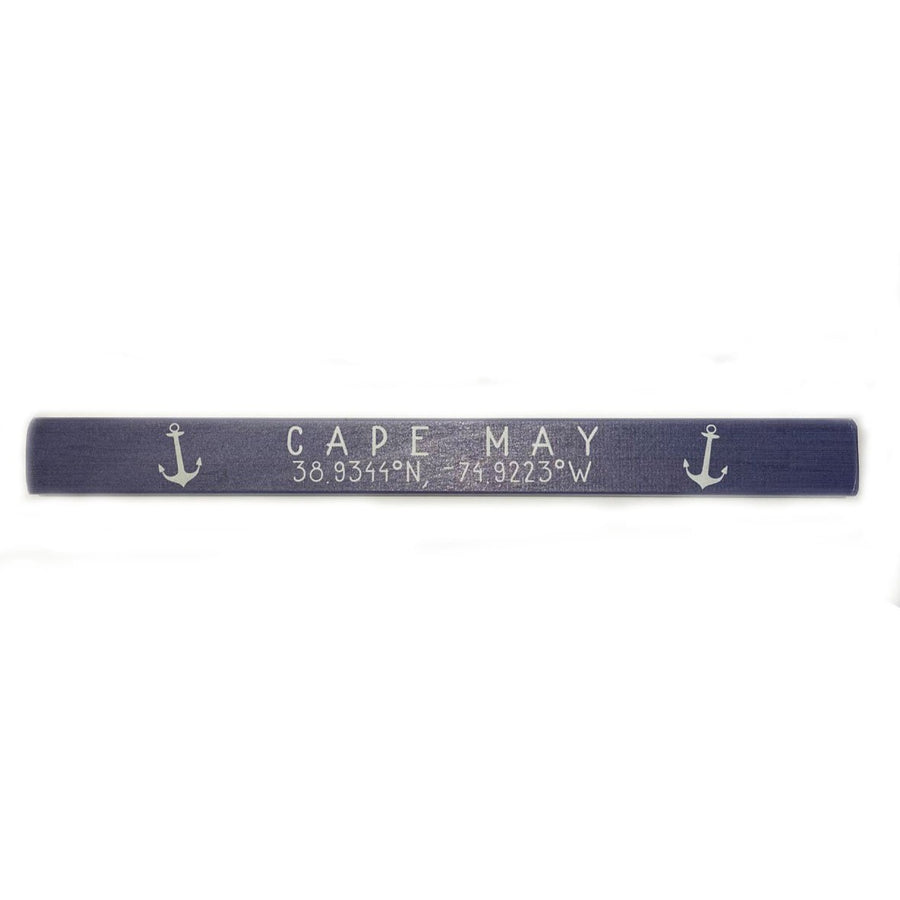 The Cape May Coordinates sign by SincereSurroundings, in navy blue wood, features "CAPE MAY 38.9341°N 74.9223°W" and small white anchors on each side, ideal for a nautical-themed shelf.