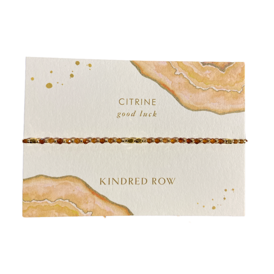 The Citrine Healing Gemstone Stacking Bracelet by Kindred Row features natural citrine beads and comes on a card with gold and amber watercolor art, reading "Citrine good luck" and "Kindred Row.